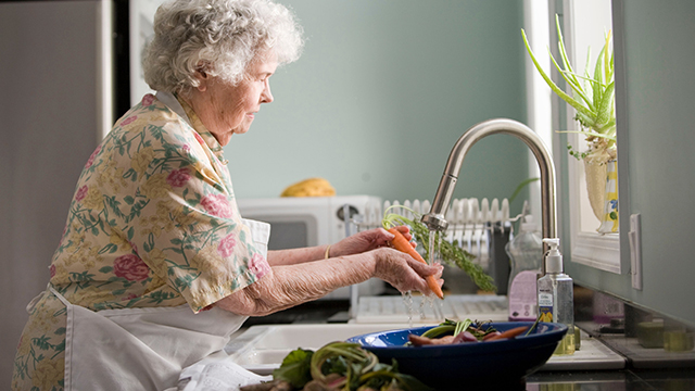 elderly woman washing carrot for cooking preparation
